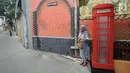 Warga bermain handphone di samping kotak telepon di Gang Kepatihan, Jalan Veteran, Kebon Kelapa, Bogor Tengah, Bogor, Jawa Barat, Jumat (15/3). Gang Kepatihan mengusung tema internasional. (merdeka.com/Arie Basuki)