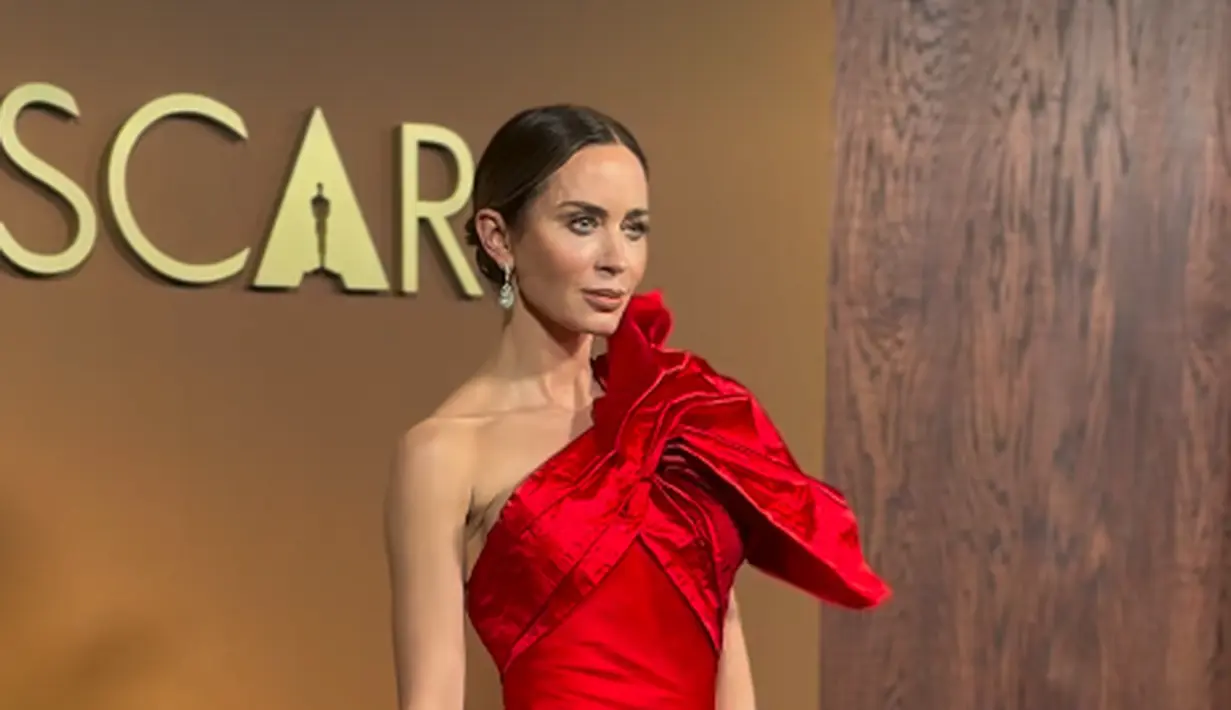 Emily Blunt tampil menyala dengan one shoulder dress beraksen pita ruffle besar dari Schiaparelli. Gaun satin merah ini memiliki aksen sheer di bagian pinggang berbentuk V [@theacademy]