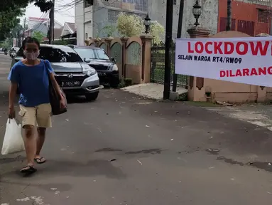 Pejalan kaki melintas di depan spanduk pemberitahuan lockdown di RT 04 / RW 09 Kelurahan Pondok Karya, Tangerang Selatan, Rabu (23/6). Melonjaknya kasus covid-19 di beberapa kawasan membuat sejumlah wilayah melakukan karantina di tingkat RT untuk memutus penyebaran corona (Liputan6.com/Angga Yuniar)