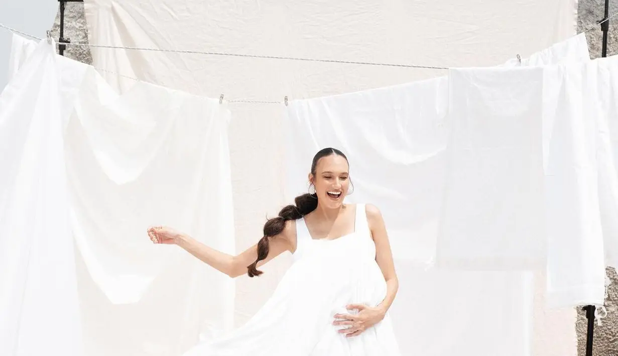 Gaya unik nan sederhana Nadine Chandrawinata lakoni maternity shoot. Nadine tampil mengenakan dress putih polos dengan latar kain-kain putih yang digantung bak cucian. [Foto: Instagram/nadinelist]