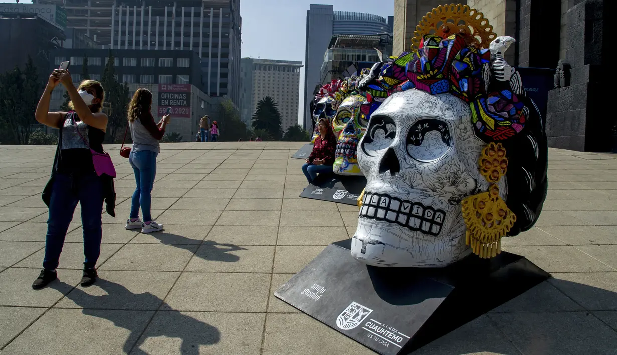 Warga berswafoto pada pameran Fridacraneos, tengkorak raksasa yang dilukis untuk menghormati mendiang seniman Meksiko Frida Kahlo, sebagai bagian dari perayaan Hari Kematian di Monumen Revolusi, Mexico City, Meksiko, 29 Oktober 2021. (Claudio CRUZ/AFP)