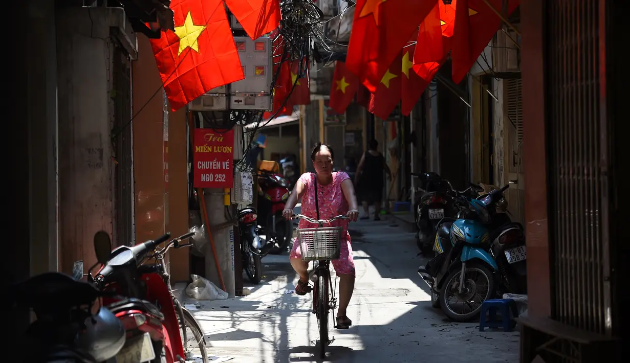 Seorang wanita mengendarai sepedanya melewati deretan bendera nasional Vietnam yang digantung di depan rumah untuk Hari Nasional Vietnam di pusat kota Hanoi (1/9/2020). Peringatan 75 tahun Hari Nasional Vietnam jatuh pada tanggal 2 September 2020. (AFP Photo/Nhac Nguyen)