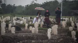 Keluarga berkumpul di dekat kuburan korban virus Corona Covid-19 di tengah hujan lebat di pemakaman Keputih, Surabaya (7/1/2020). Data Surabaya Lawan Covid-19 per 5 Januari 2021 menyebutkan, ada kenaikan 0.27 persen sehingga total kasus positif di Surabaya menjadi 18.399 kasus. (AFP/Juni Kriswanto)