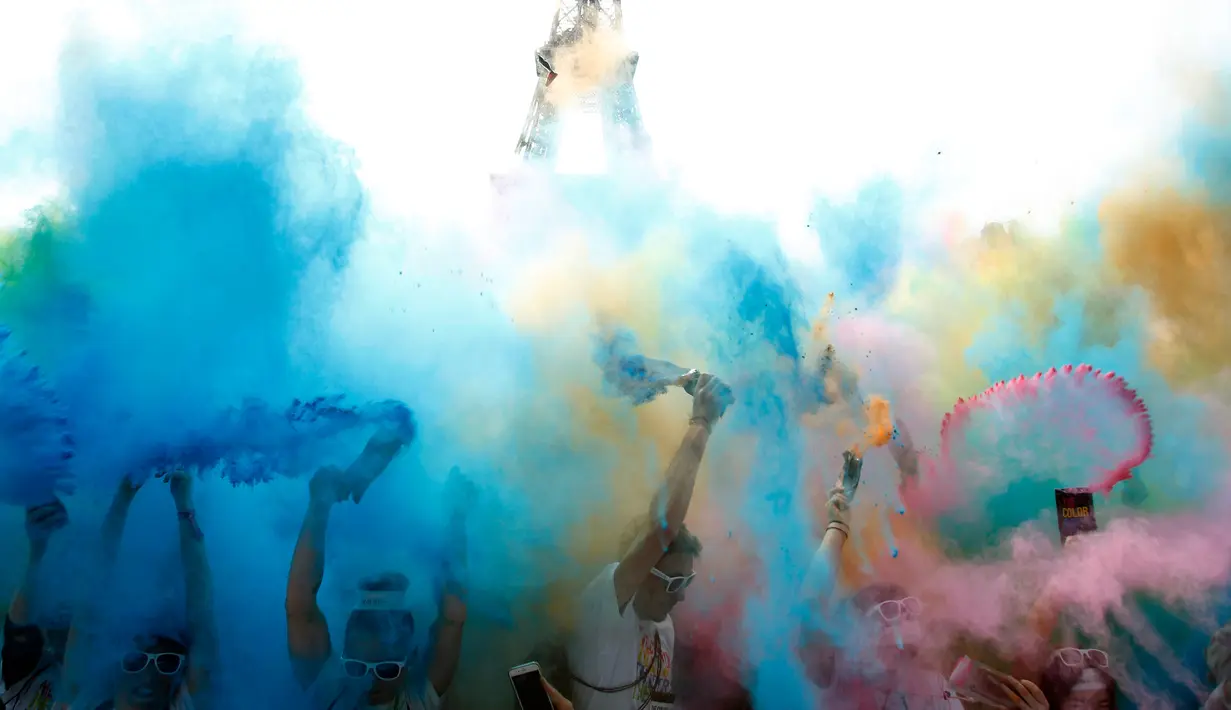 Sejumlah orang melempar bubuk berwarna saat merayakan akhir perlombaan Color Run 2018 di depan Menara Eiffel di Paris, Prancis (15/4). Acara lari 5 kilometer ini diakhiri dengan saling lempar bubuk berwarna antar peserta. (AP/Thibault Camus)