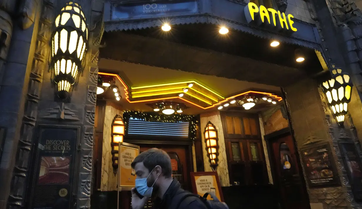 Seorang pria bermasker berjalan melewati sebuah bioskop art deco di Amsterdam, Sabtu (18/12/2021). Pemerintah Belanda akan melakukan penguncian ketat atau lockdown selama periode Natal dan Tahun Baru untuk mencoba menahan varian covid-19 Omicron yang sangat menular. (AP Photo/Peter Dejong)