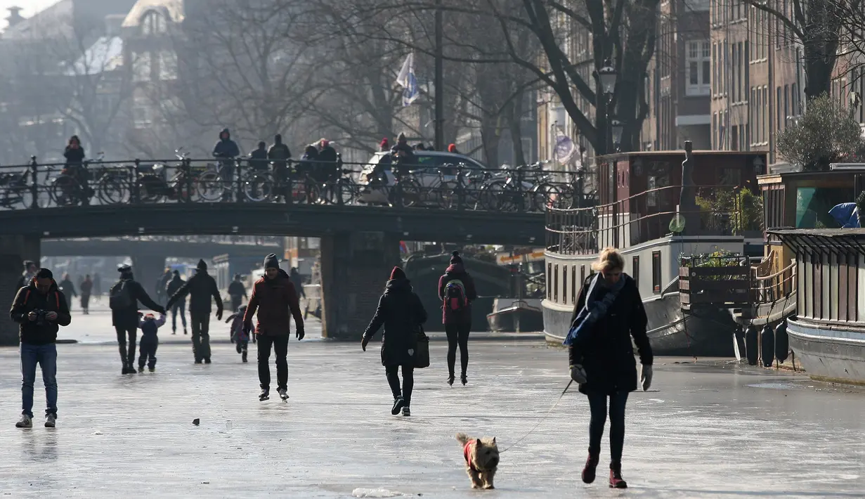 Seorang wanita membawa anjingnya berjalan melintasi permukaan kanal Prinsengracht yang membeku di Amsterdam, Belanda, Jumat (2/3). Untuk pertama kalinya dalam enam tahun, bagian kanal bersejarah di Amsterdam tersebut membeku. (AP/Mike Corder)