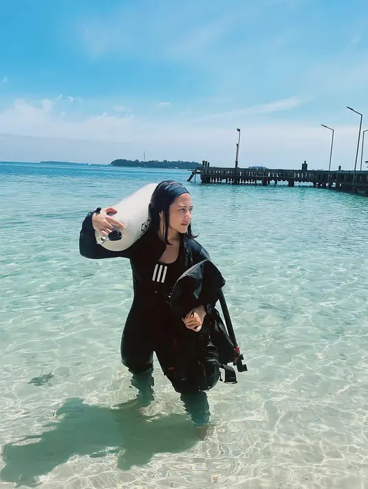 Melihat Prilly bergaya di pantai dengan outfit diving yang lengkap. Bodysuit lengkap berwarna hitam, Prilly berpose memanggul tabung oksigen di bahunya. Foto: Instagram.