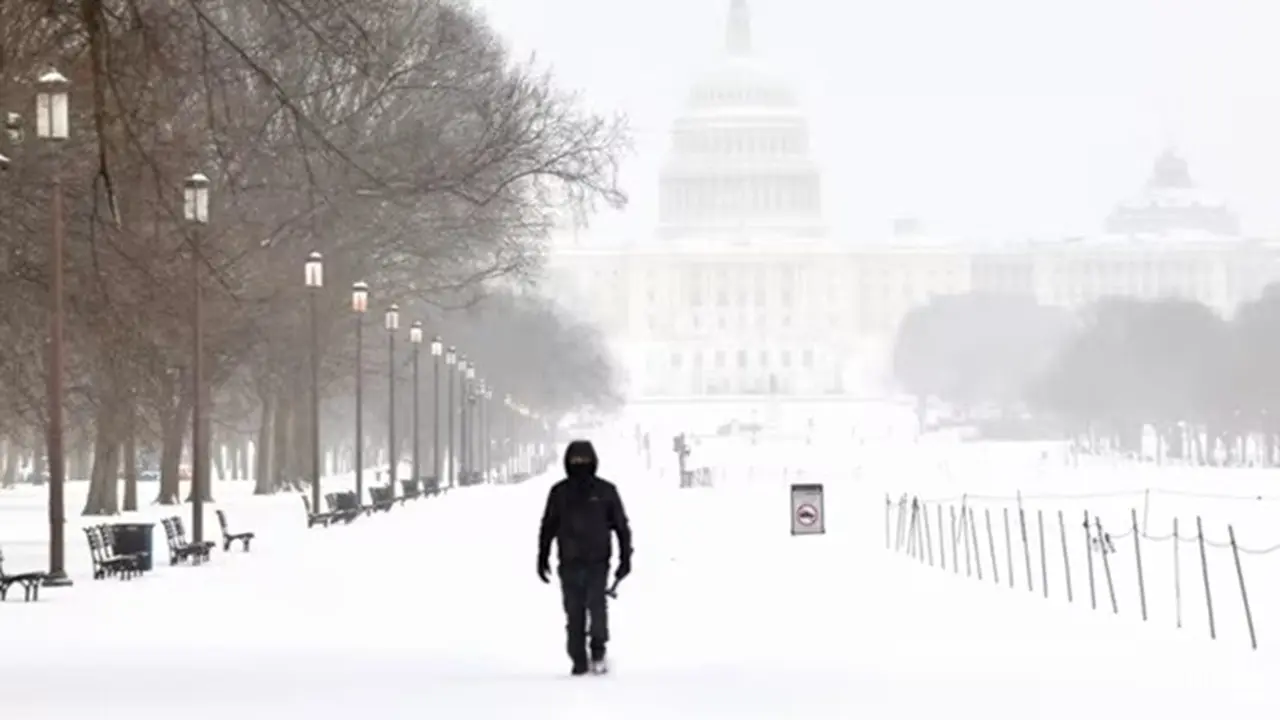 Seorang pria berjalan di kawasan National Mall saat salju turun di Washington, pada Minggu (25/1/2026).