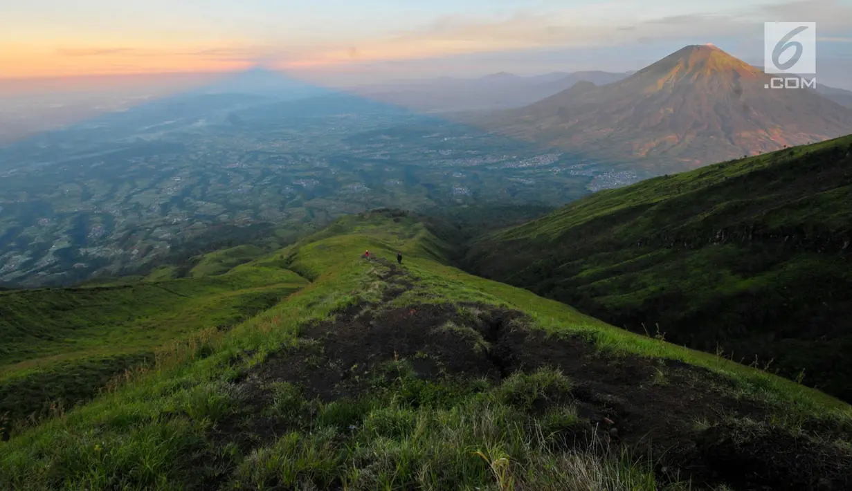Pendaki terlihat dari kejauhan saat mendaki menuju puncak Sumbing dengan latar belakang pemandangan Gunung Sindoro dan pegunungan lainnya pada pagi hari di Wonosobo, Jawa Tengah (3/4). (merdeka.com/Iqbal S. Nugroho)