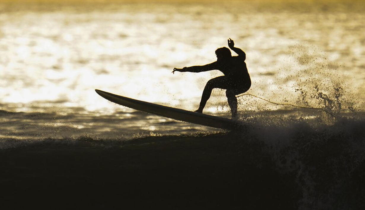 Seorang peselancar mengendarai ombak di Huntington Beach, California, Amerika Serikat, 12 Januari 2022. Peselancar di seluruh California Selatan berbondong-bondong ke daerah pantai saat gelombang ombak besar memasuki wilayah tersebut. (AP Photo/Ashley Landis)
