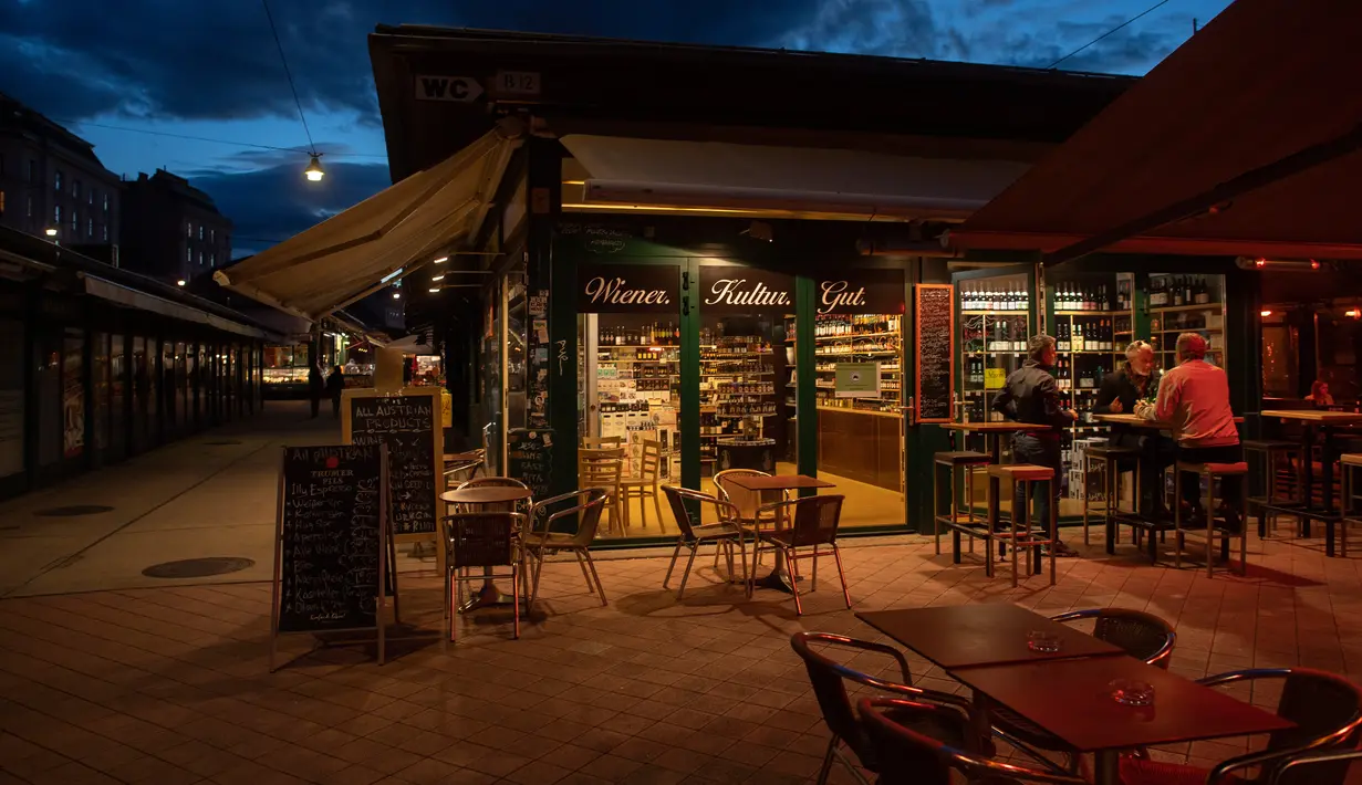 Orang-orang minum di pasar Naschmark yang biasanya penuh sesak di Wina, Austria pada 5 Oktober 2020. Naschmarkt adalah pasar tertua, terbesar, dan terpopuler di Wina kini sepi pengunjung akibat pandemi corona COVID-19. (JOE KLAMAR / AFP)