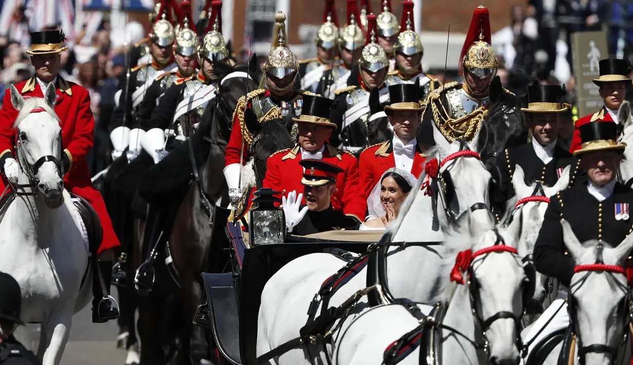 Pangeran Harry dan sang istri, Meghan Markle malambaikan tangan kepada warga saat menaiki kereta kencana setelah upacara pernikahan mereka di Kastil Windsor, Inggris, Sabtu (19/5). (Adrian DENNIS/AFP)