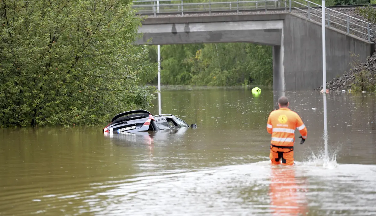 Personel penyelamat mendekati mobil yang terendam air banjir di jalan utama di Falun, Swedia, Rabu (18/8/2021). Hujan deras di Swedia timur telah menggenangi beberapa area pemukiman, dengan beberapa jalan dan jembatan tergenang saat hujan terus turun. (Ulf Palm / TT via AP)