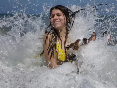 Mariana Rojas dan anjingnya bermain ombak di lepas pantai Los Angeles setelah dibuka kembali di La Guaira, Venezuela, Jumat (23/10/2020). Pemberlakuan lockdown yang ketat akibat COVID-19 memaksa penutupan pantai di seluruh negeri pada Maret lalu dan dibuka kembali minggu ini. (AP/Matias Delacroix)