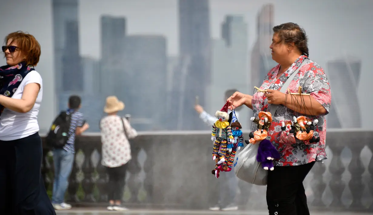 Seorang pedagang saat berjualan boneka di bukit Vorobyovy, Rusia (12/7). Dengan berpose di perbukitan Vorobyovy pengunjung dan wisatawan bisa mengambil latar belakang kota di Moskow. (AFP Photo/Alexander Nemenov)