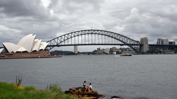 Dua pelari beristirahat di Kursi Nyonya Macquarie yang menghadap ke Opera House dan Harbour Bridge di Sydney, Rabu (30/12/2020). Klaster baru virus korona (Covid-19) muncul di kota Sydney, New South Wales, Australia, menjelang pergantian tahun. (Saeed KHAN / AFP)