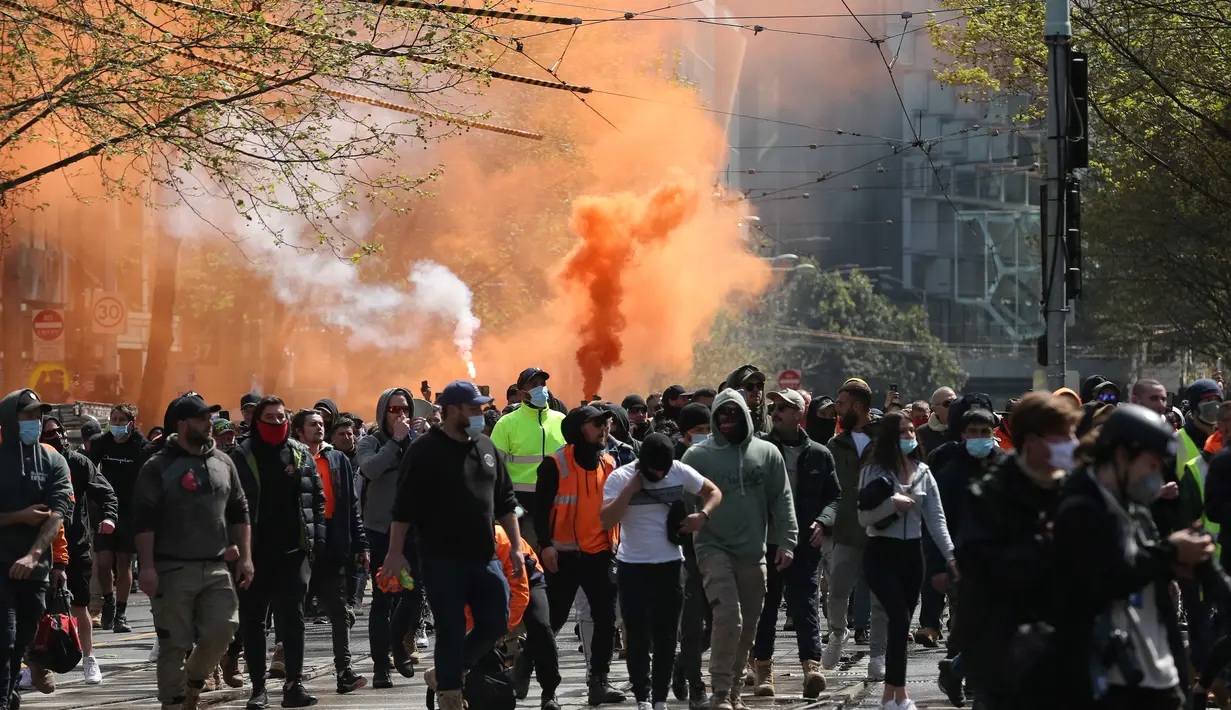 Suar dinyalakan ketika pekerja konstruksi dan demonstran menghadiri protes terhadap peraturan Covid-19 di Melbourne (21/9/2021). Polisi telah menangkap setidaknya 44 orang setelah adegan liar, di mana beberapa petugas diduga terluka. (AFP/Con Chronis)