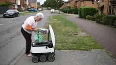 Sheila (71) mengambil kiriman dari robot otonom bernama Starship yang mengantarkan bahan makanan dari supermarket Co-op di Milton Keynes, Inggris, 20 September 2021. Robot Starship bertugas mengantarkan belanja dan makanan. (DANIEL LEAL-OLIVAS/AFP)