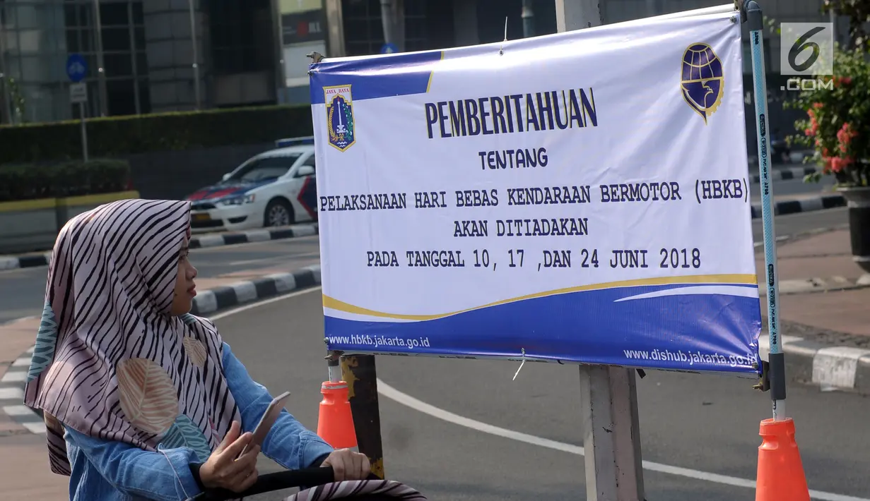 Warga melihat spanduk pemberitahuan peniadaan pelaksanaan Hari Bebas Kendaraan Bermotor (HBKB) di sekitar Bundaran Hotel Indonesia, Jakarta, Minggu (3/6). Pelaksanaan HBKB akan ditiadakan pada 10, 17, dan 24 Juni 2018. (Liputan6.com/Helmi Fithriansyah)