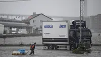 Seorang pria berjalan di sepanjang Fiskhamnen (pelabuhan nelayan) yang banjir setelah sungai Gota Alv meluap akibat hujan deras di Gothenburg, Swedia, Selasa, 8 Agustus 2023.  (Björn Larsson Rosvall/TT News Agency via AP)