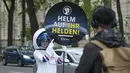 Seorang siswa berkostum astronaut memperlihatkan peringatan kepada pengendara sepeda untuk mengenakan helm di Ring Street, Wina, Austria, Rabu (5/5/2021). Delapan siswa Wina berpartisipasi dalam acara tersebut untuk mengingatkan pengendara sepeda mengenakan helm demi keamanan mereka (JOE KLAMAR/AFP)