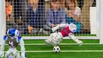 Robot penjaga gawang tim 'Nomadz' Swiss berhasil menahan bola saat melawan robot tim 'Hulk' dari Jerman dalam pertandingan kompetisi Liga Platform Standar di RoboCup GermanOpen 2018, Magdeburg, Jerman (28/4). (AP/Jens Meyer)