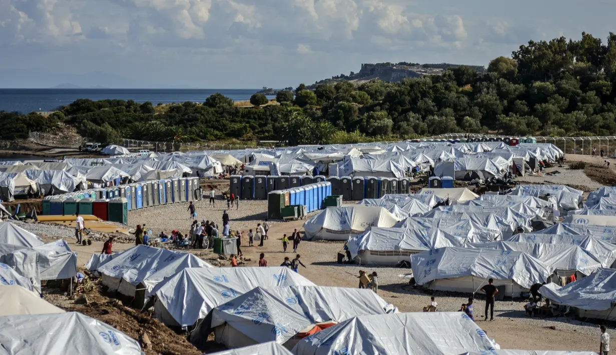 Para migran mengisi air sementara yang lain membersihkan barang-barang mereka setelah hujan badai di kamp pengungsi Kara Tepe, di timur laut pulau Lesbos, Yunani (14/10/2020). (AP Photo/Panagiotis Balaskas)
