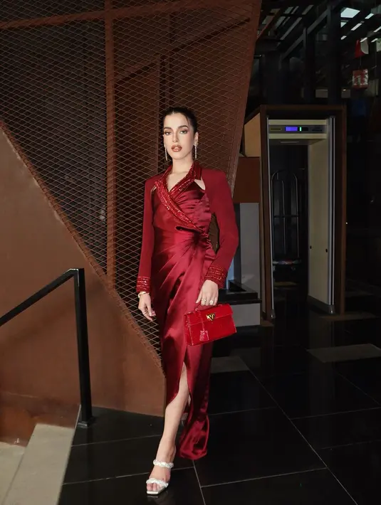 Tasya Farasya tampil anggun dan berani dalam balutan gaun satin merah yang berkilauan, memberikan sentuhan glamor dan elegan. Gaun tersebut dilengkapi dengan detail kerah dan pergelangan tangan yang dihiasi manik-manik, menciptakan tampilan yang mewah dan berkelas. Sebagai pelengkap penampilannya, Tasya membawa tas jinjing merah model croco yang memberikan kesan eksklusif dan tegas.[IG/@tasyafarasya].