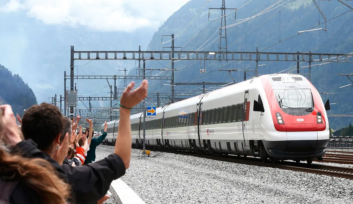 Pengunjung melambaikan tangan ke arah kereta api yang melintasi terowongan Gotthard di kota Erstfeld, Swiss, Rabu (1/6). Swiss resmi membuka terowongan kereta api terpanjang, yang membentang sepanjang 57 km di bawah Pegunungan Alpen. (REUTERS/SRG/Pool)