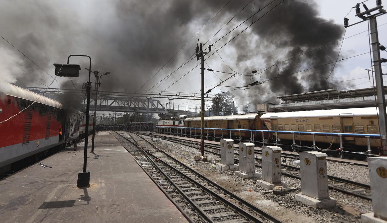 Asap mengepul dari kereta api yang dibakar pengunjuk rasa di stasiun kereta api Secundrabad di Hyderabad, India, Jumat (17/6/2022). Ratusan pemuda melampiaskan kemarahan dengan membakar gerbong kereta, merusak properti kereta api dan memblokir rel dan jalan raya dengan batu-batu besar sebagai serangan balasan. (AP Photo/Mahesh Kumar A)