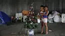 Camila (kanan) dan anaknya berpose disamping pohon Natal di Sao Paulo, Brasil, (18/12). Mereka adalah keluarga tunawisma yang tinggal di bawah jembatan. (REUTERS/Nacho Doce)
