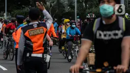 Petugas mengatur lalu lintas saat warga bersepeda di kawasan Thamrin, Jakarta Pusat, Minggu (15/11/2020). Di masa PSBB transisi Jakarta, warga tetap melakukan aktivitas olahraga, khususnya bersepeda yang kini banyak diminati bahkan menjadi tren. . (Liputan6.com/Johan Tallo)