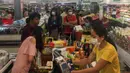 Orang-orang antre untuk membayar makanan dan belanjaan lainnya di supermarket 24 jam di Yangon, Selasa (24/3/2020). Tanggapi kasus pertama Corona COVID-19 pada Senin 23 Maret malam, warga Myanmar memadati pusat perbelanjaan untuk menyetok kebutuhan pokok dan persedian makanan. (AP/Thein Zaw)