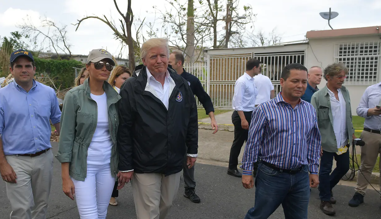 Presiden AS Donald Trump dan ibu negara Melania Trump berkeliling ke permukiman yang terdampak Badai Maria di Guaynabo, Puerto Rico, Selasa (3/10). Akan tetapi, dalam kunjungan itu Melania terlihat menggunakan celana jins berwarna putih. (MANDEL NGAN/AFP)