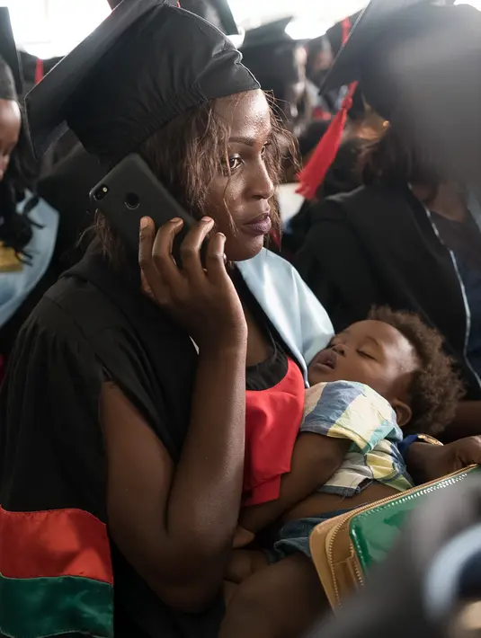 Seorang wisudati membawa anaknya saat mengikuti upacara wisuda ke-68 di Universitas Makerere di Kampala, Uganda (19/1). Sebanyak lebih dari 14.000 mahasiswa menerima gelar dari Universitas Makerere. (AFP Photo/Michele Sibiloni)