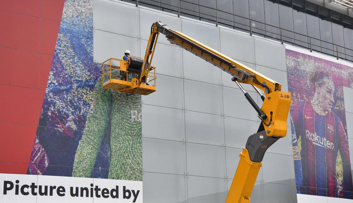 Pekerja melepas poster yang menampilkan pemain depan Argentina, Lionel Messi di pintu masuk Stadion Camp Nou, Barcelona pada Selasa, 10 Agustus 2021. Lionel Messi resmi meninggalkan Barcelona akibat masalah finansial klub dan peraturan dari Liga Spanyol. (AFP/Pau Barrena)