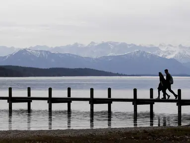 Pasangan berjalan di dermaga di depan pegunungan Alp di danau Starnberger See dekat desa Starnberg, Jerman selatan, selama cuaca musim semi dengan suhu 15 derajat pada 3 April 2018. (AFP Photo/Christof Stache)