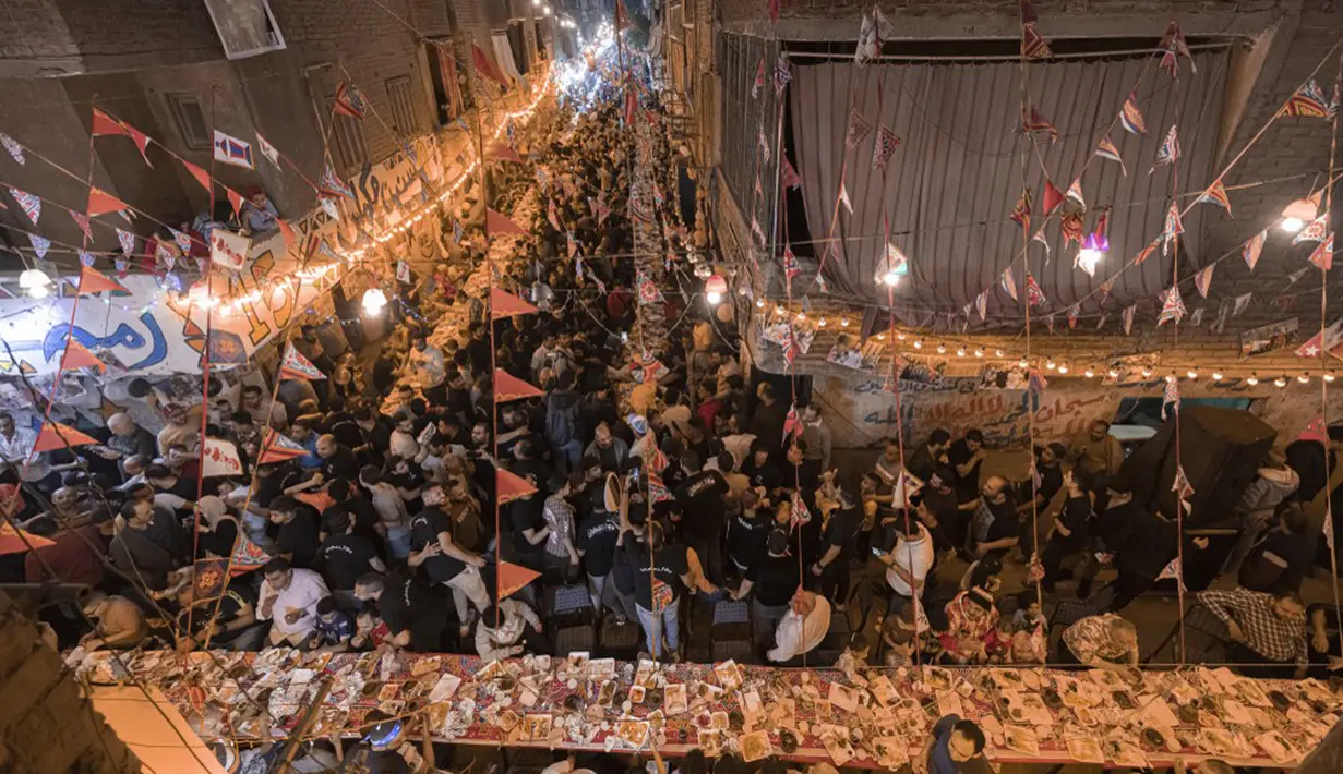Umat muslim berkumpul di meja sepanjang jalan untuk berbuka puasa bersama dalam jamuan buka puasa massal pada hari ke-15 bulan suci Ramadhan di pinggiran Matariya, timur laut Kairo, Mesir, 16 April 2022. (Khaled DESOUKI/AFP)