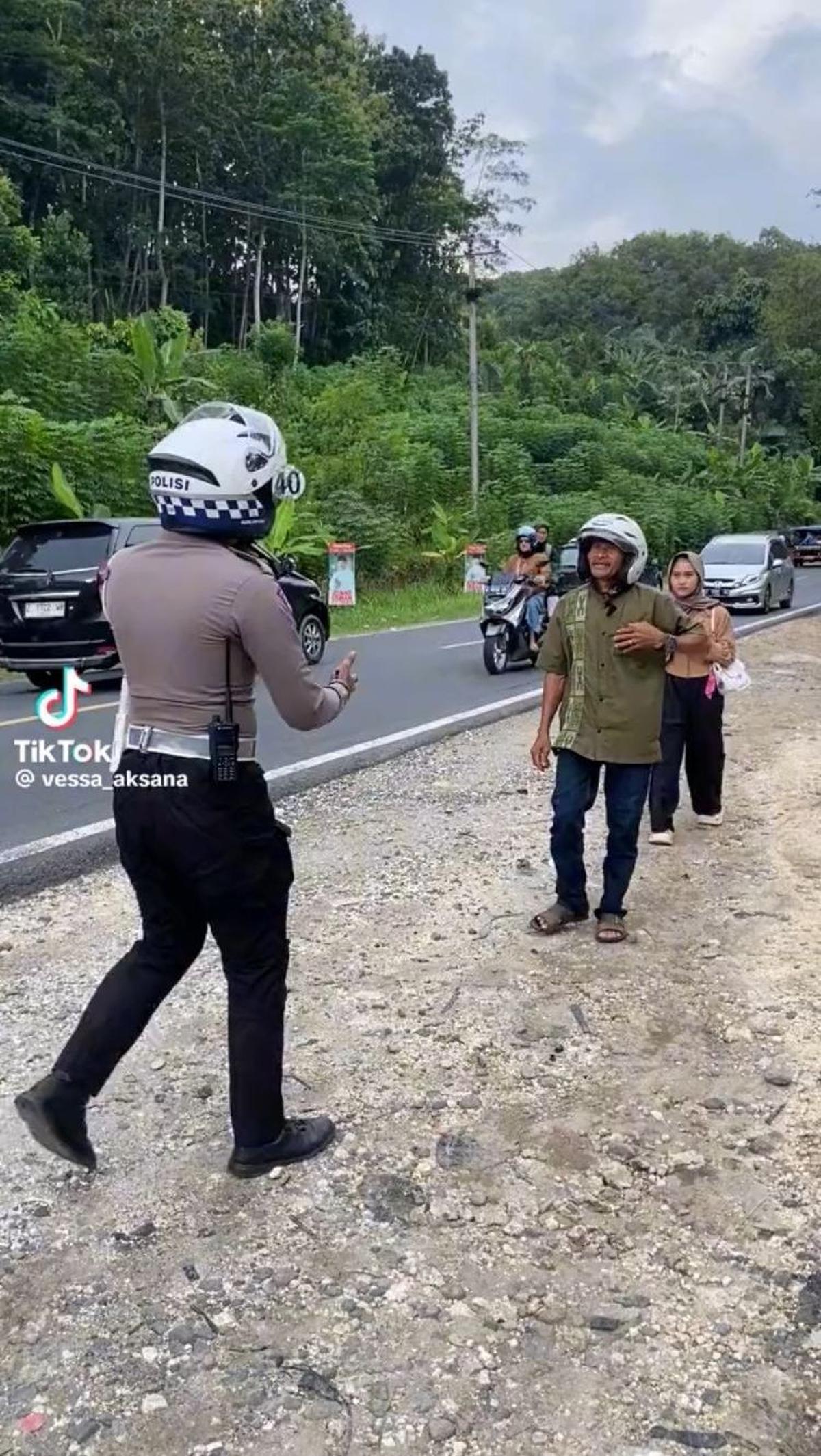 Awalnya, seorang bapak dan anaknya turun dari motor karena motor mereka mengalami masalah. Seorang petugas polisi pun langsung menghampiri bapak dan anak ini.