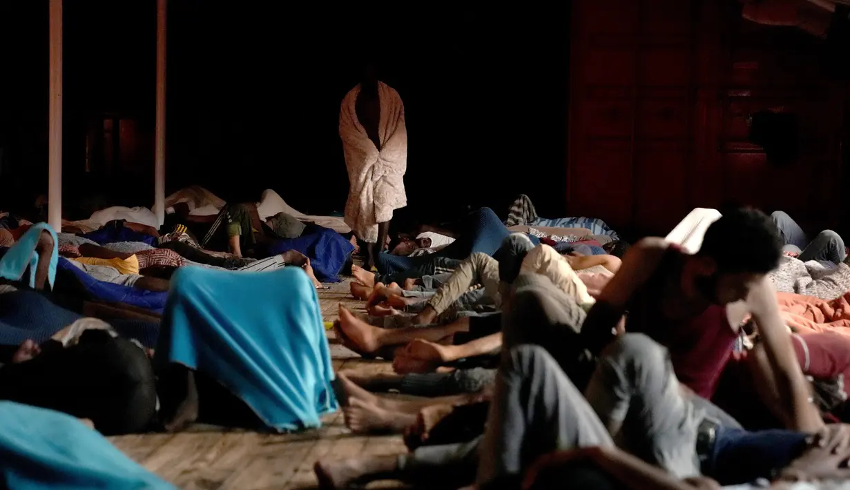 Seorang migran terbungkus selimut ketika yang lain tidur di dek kapal penjaga pantai LSM Spanyol Open Arms setelah mereka diselamatkan dari perairan terbuka selama operasi di zona perairan internasional, di laut Mediterania, Selasa pagi, 20 September 2022. (AP/Petros Karadjias)
