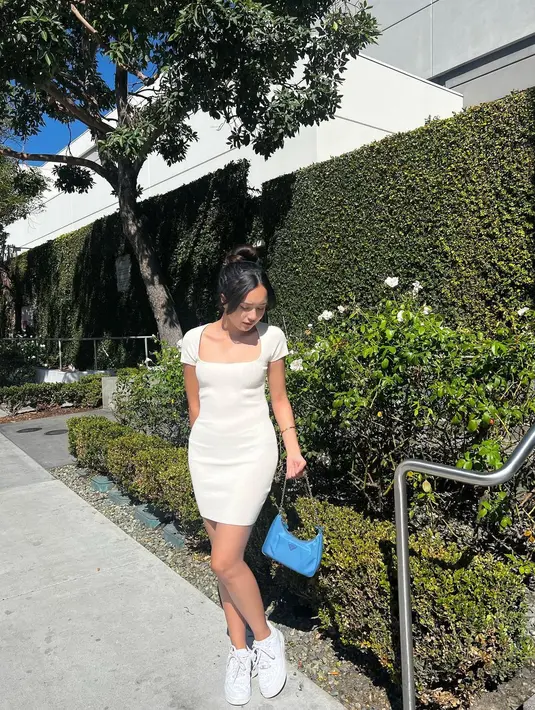 Beby Tsabina berpose sambil menenteng tas berwarna biru dengan memakai sneaker berwarna putih senada dengan dress yang ia kenakan. (Instagram/bebytsabina)