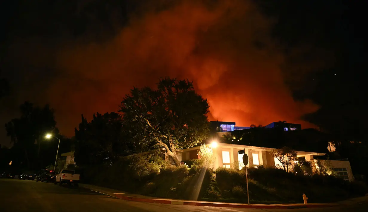 Kepulan asap dan kobaran api dari Kebakaran Palisades membakar di belakang sebuah rumah di jalan Corda menuju lingkungan Encino di Los Angeles, California, Amerika Serikat, 10 Januari 2025. (Patrick T. Fallon/AFP)