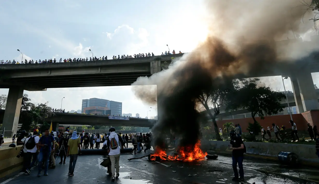 Demonstran dari oposisi membakar ban dan memblokir sebuah jalan di Caracas, Venezuela (24/4). Protes yang terjadi di seluruh Venezuela ini diperkirakan menjadi yang terbesar dalam tiga tahun. (AP Photo/Ariana Cubillos)