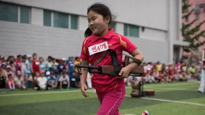 Seorang anak gadis membawa senapan mainan dan berusaha melewati rintangan (AFP)