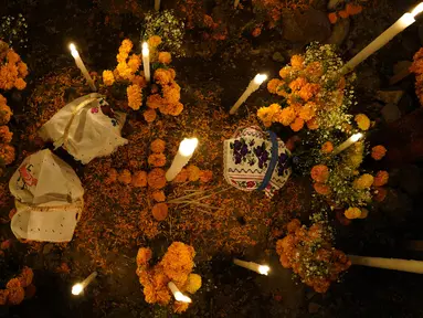 Bunga, persembahan makanan, dan lilin menghiasi makam pada perayaan Hari Kematian di pemakaman Arocutin, Michoacan, Meksiko, 1 November 2021. Pada Hari Kematian, kerabat menghabiskan malam di samping makam orang yang mereka cintai. (AP Photo/Eduardo Verdugo)