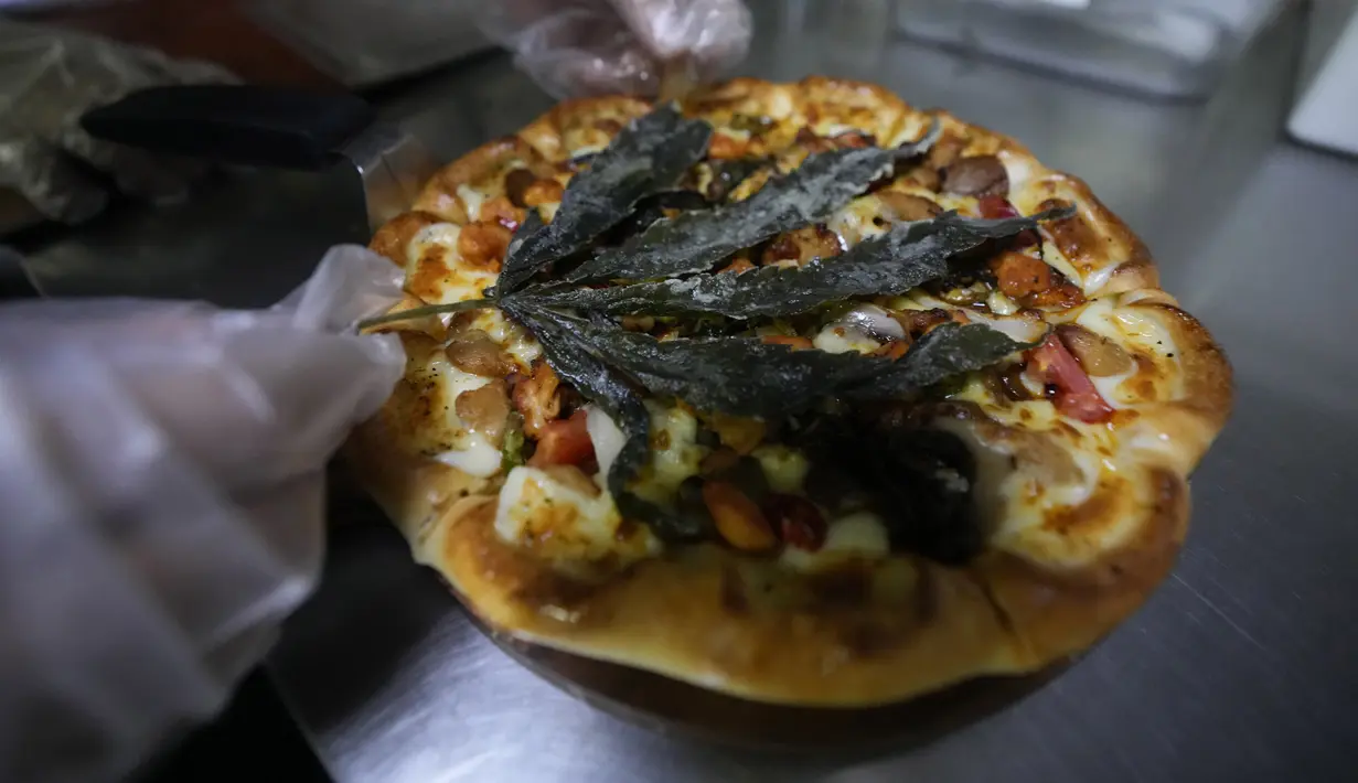 Seorang pekerja menghias pizza dengan daun ganja goreng di sebuah restoran di Bangkok, pada 24 November 2021. The Pizza Company, jaringan makanan cepat saji utama Thailand memperkenalkan makanan andalannya bulan ini, yakni pizza ganja berjuluk ‘Crazy Happy Pizza’. (AP Photo/Sakchai Lalit)
