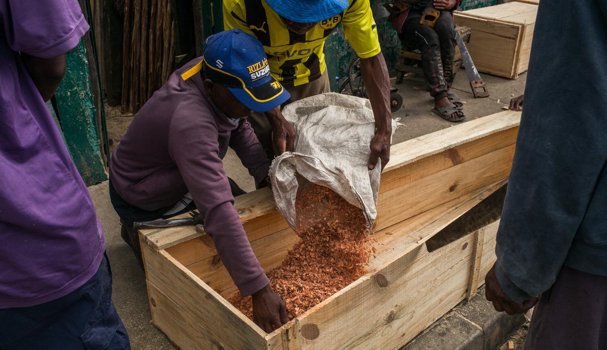 Mr. Jean melempar serbuk gergaji ke dalam peti mati saat bersama timnya membuat peti mati murah di jalan di Antananarivo, Rabu (14/4/2021). Sejak gelombang kedua Covid-19 di Madagaskar, yang menyebabkan jumlah kematian meningkat di ibu kota, permintaan peti mati juga meningkat pesat. (RIJASOLO/AFP)