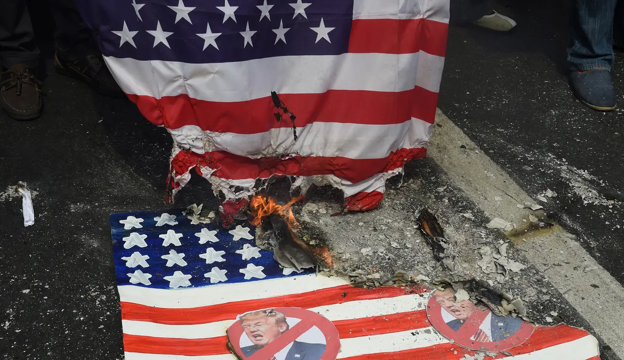 Bendera AS dengan wajah Presiden saat dibakar oleh pengunjuk rasa di depan kedutaan AS, Manila, Filipina (20/1). Donald Trump akan menjadi Presiden AS ke-45 yang akan dilantik pada 20 Januari 2017. (AFP Photo/Ted Aljibe)