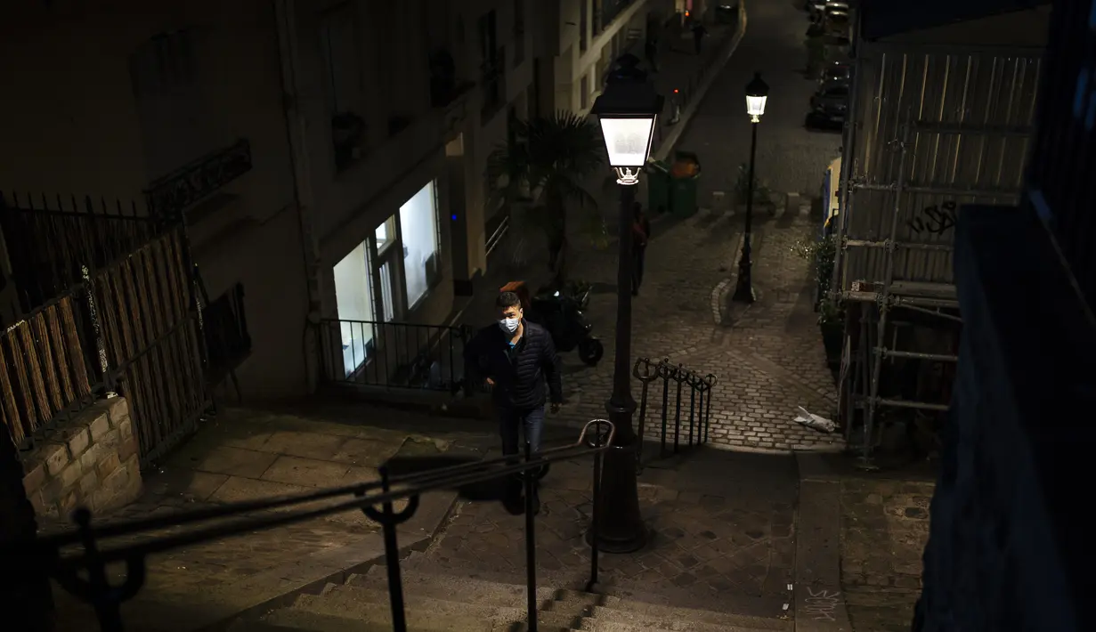 Seorang pria memakai masker berjalan di daerah Montmartre di Paris, Jumat (30/10/2020). Prancis memberlakukan kembali penguncian nasional selama sebulan yang bertujuan untuk memperlambat penyebaran virus, menutup semua bisnis yang tidak penting. (AP Photo/Lewis Joly)