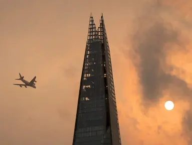 Sebuah pesawat melintas di atas gedung pencakar langit The Shard di pusat kota London, Senin (16/10). Beberapa area menunjukkan langit di London berubah warna menjadi kemerahan, kekuningan, bahkan ada yang kecokelatan. (Dominic Lipinski/PA via AP)